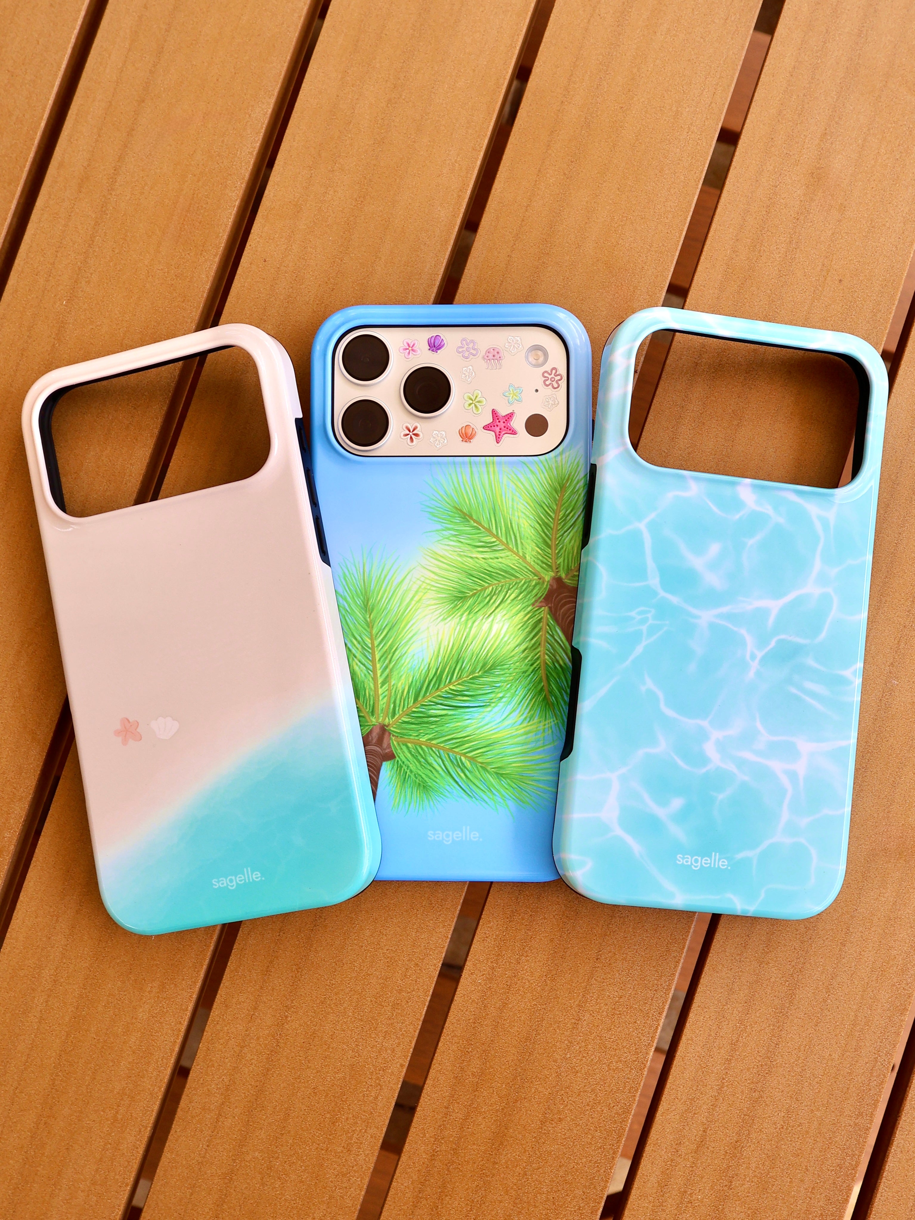 Three phone cases with different beach designs on a wooden surface